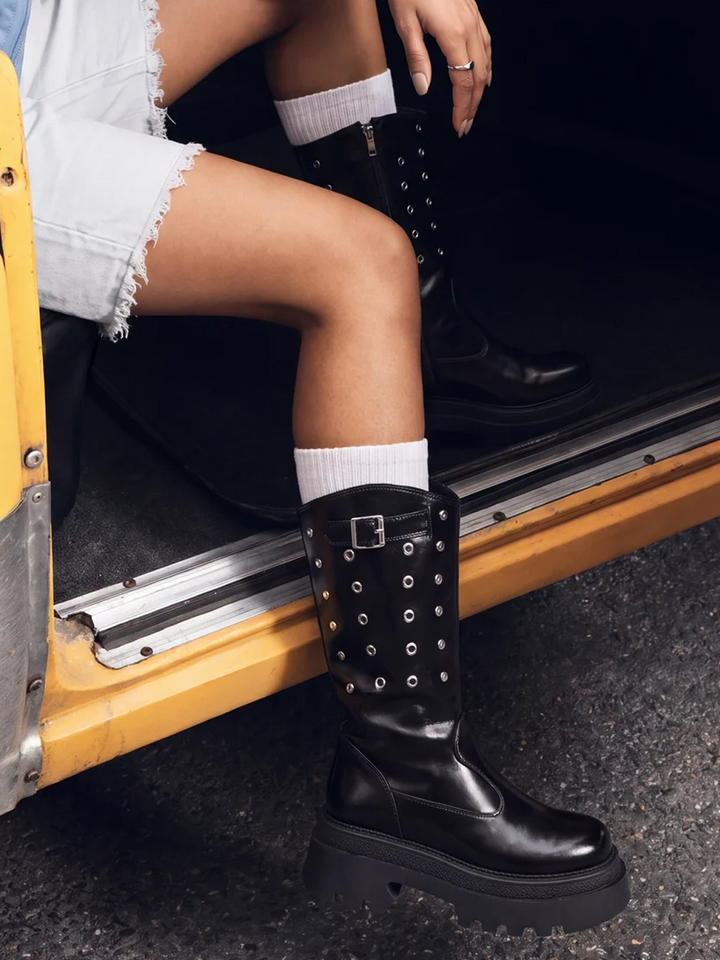 Black faux leather eyelet platform mid-calf boot – worn on model with white socks in a taxi