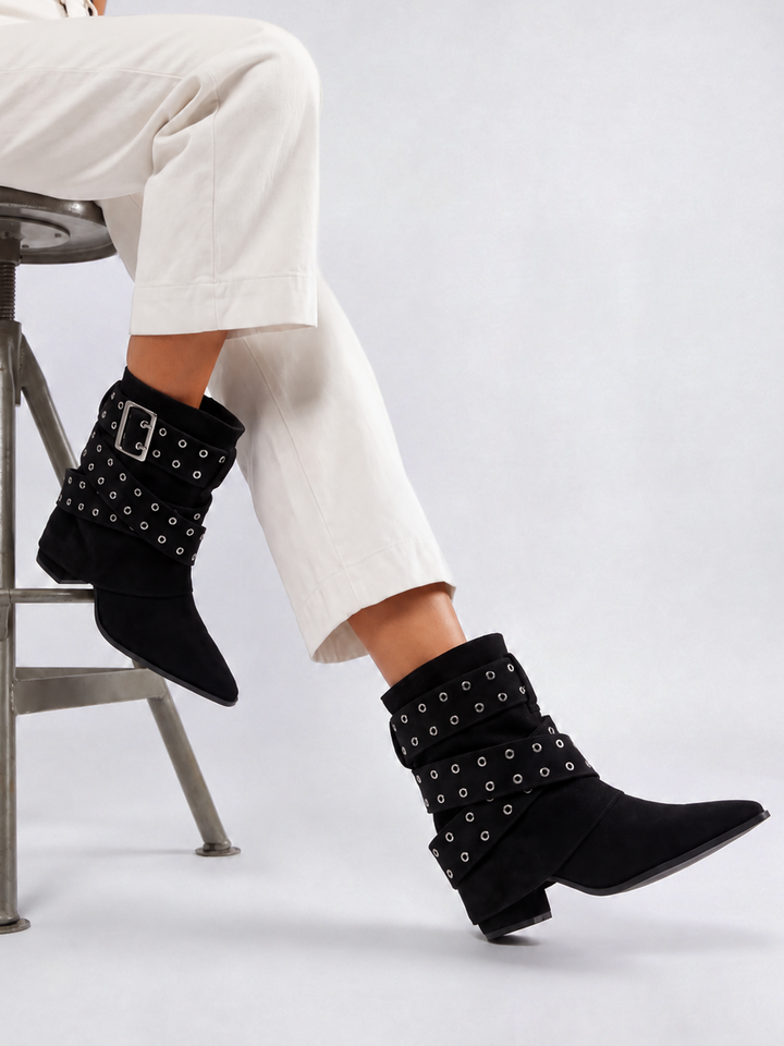 Black faux suede buckle strap slouch ankle boot – worn on model, seated, side view