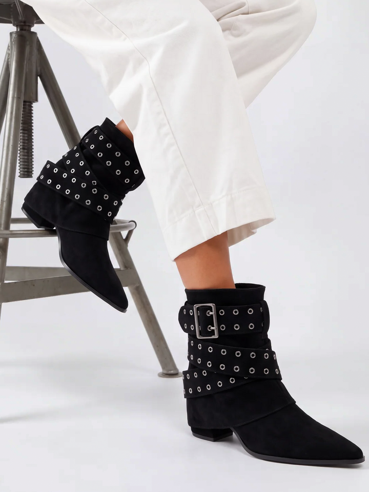Black faux suede buckle strap slouch ankle boot – worn on model, seated, three-quarter view