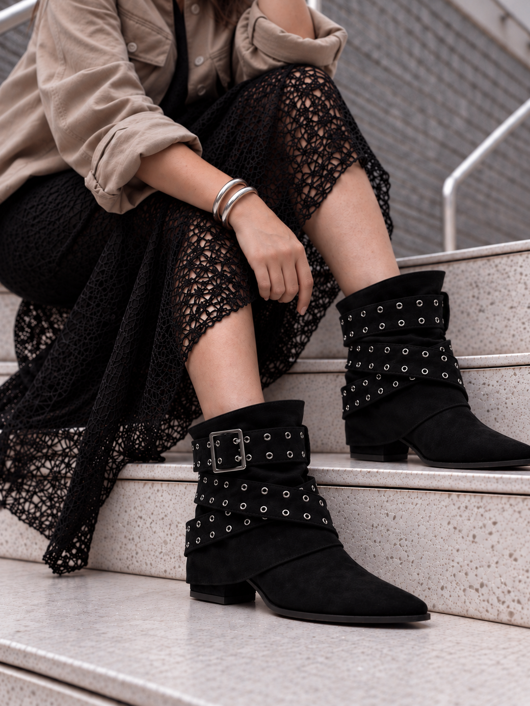 Black faux suede buckle strap slouch ankle boot – worn on model on steps, close-up