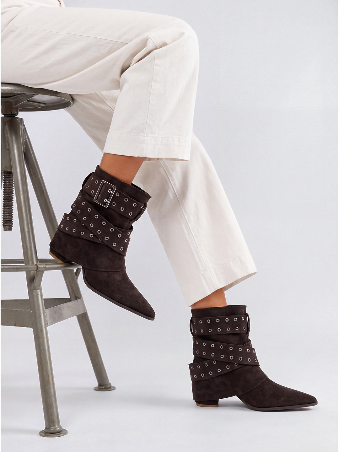 Brown faux suede buckle strap slouch ankle boot – worn on model, seated on a stool