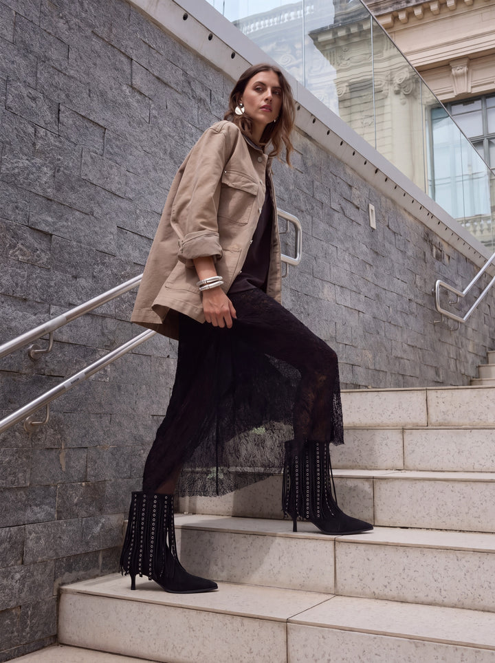 Black faux suede fringe heeled ankle boot – full outfit on model on city steps