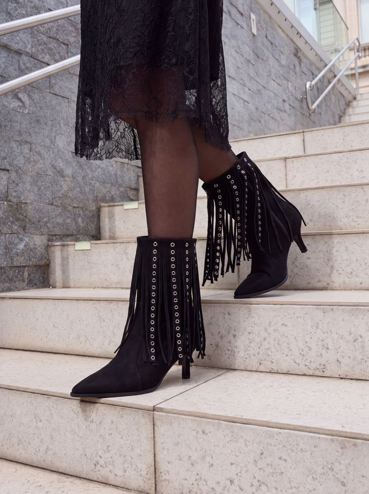Black faux suede fringe heeled ankle boot – worn on model on city steps